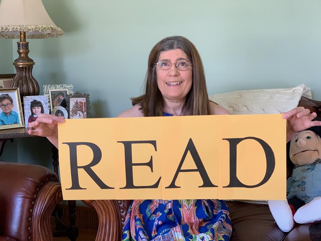 Picture of Miss Nuccia holding a sign that says Read